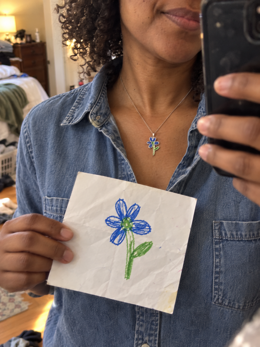 Woman wearing a blue flower pendant while holding the child's flower drawing