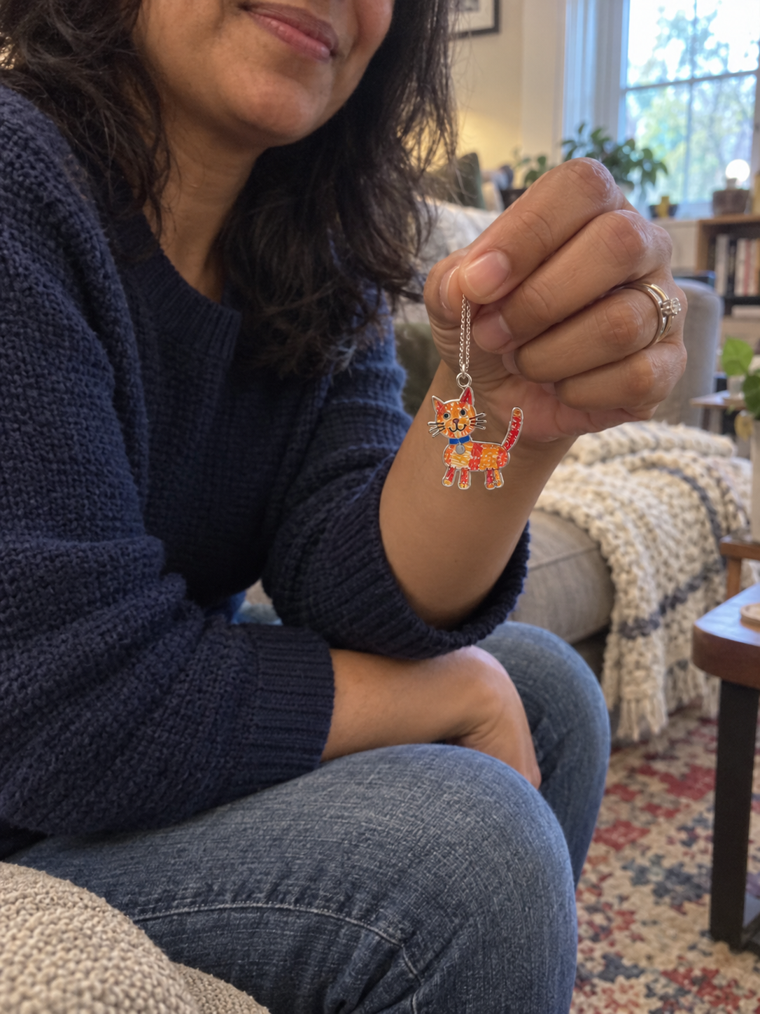 Woman holding a colorful cat pendant made from a child's drawing