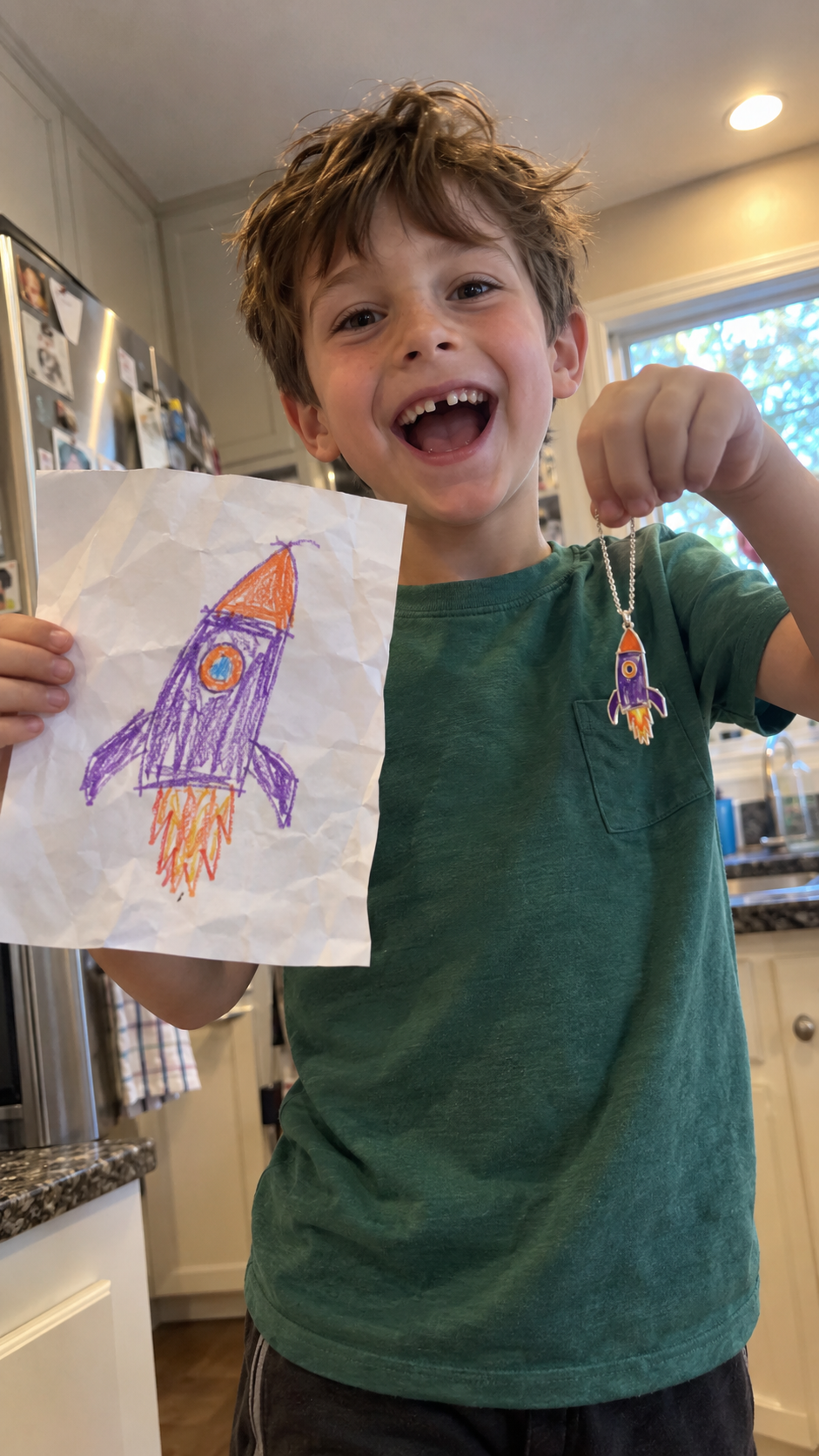 A smiling boy holding his rocket drawing next to the matching necklace