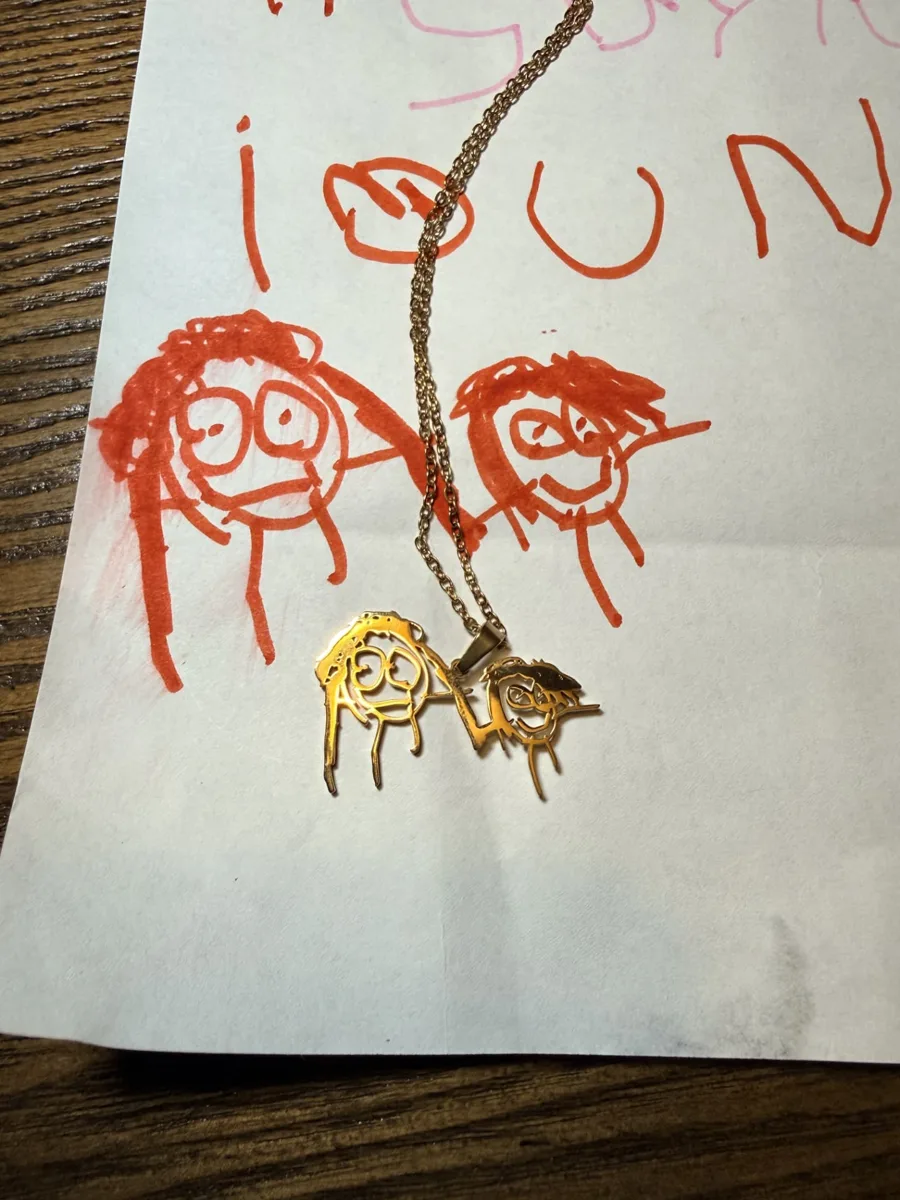 The goddaughter's orange marker drawing of two faces with the matching gold cut-out necklace laid on top