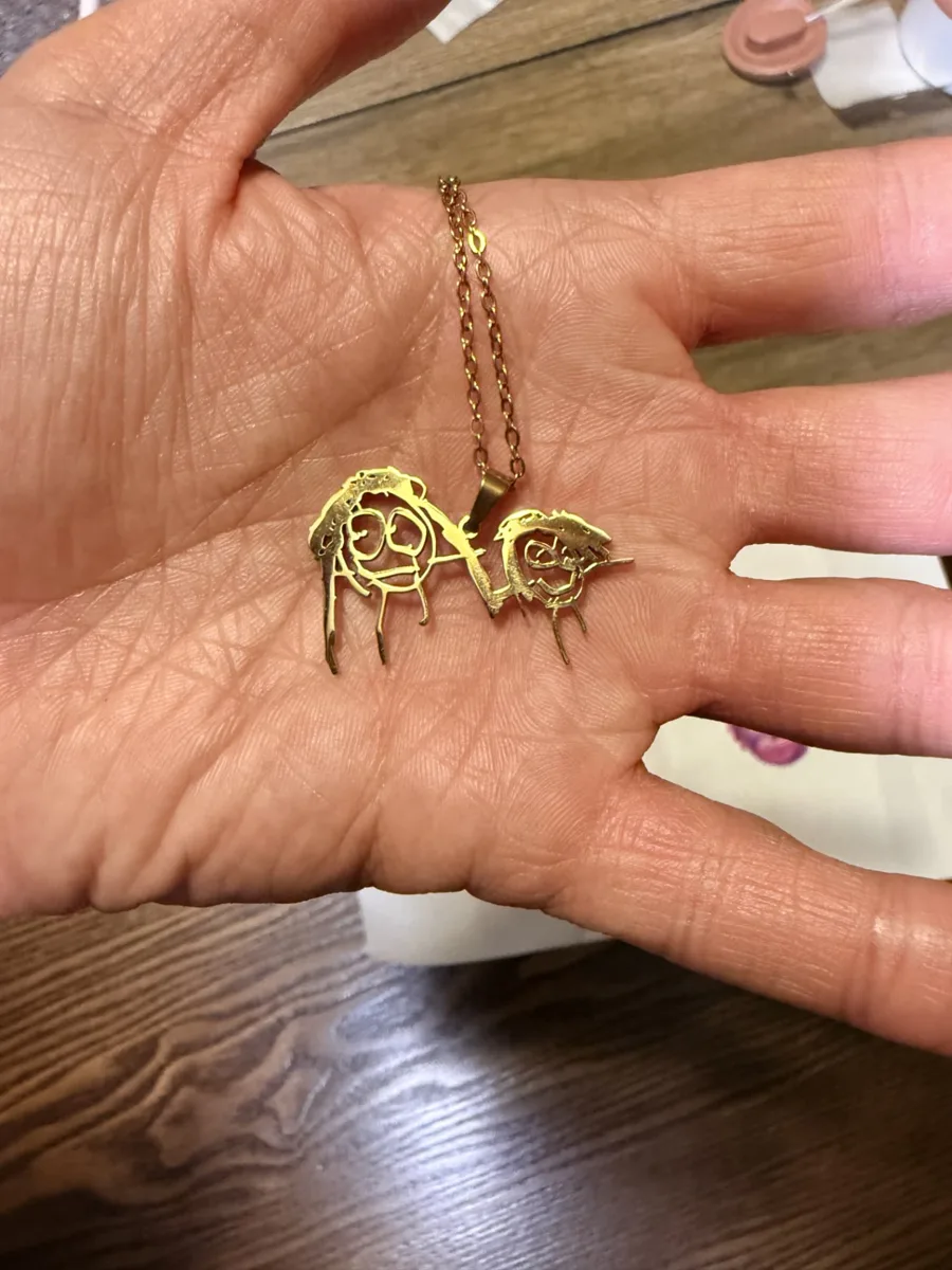 The gold cut-out necklace of two drawn faces held in an open palm